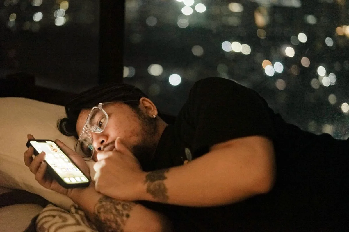 Man lying in bed at night looking at his phone, his face lit by the screen